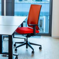 Roter ergonomischer Stuhl an Schreibtisch vor bodentiefem Fenster im Arbeitsraum