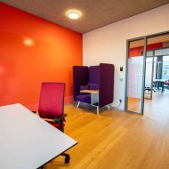 Arbeitsraum mit roter Wand, Bürostuhl, Tisch und schallgedämmter Sitzkabine.