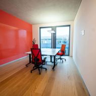 Heller Büroraum mit drei ergonomischen Stühlen, großem Tisch, roter Wand und Fensterfront