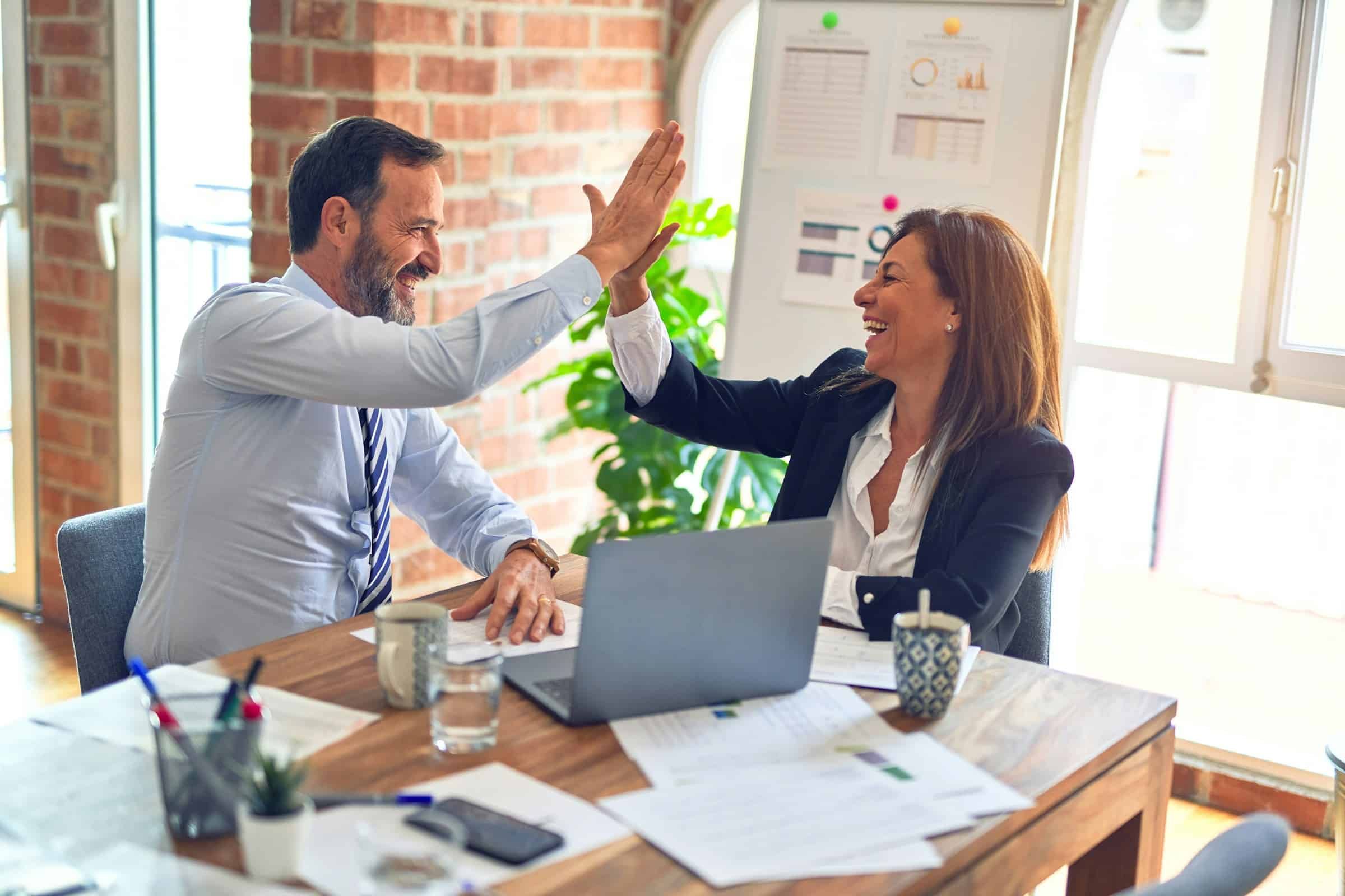 Stockfoto - Personen an Büroschreibtisch mit Laptop klatschen ein